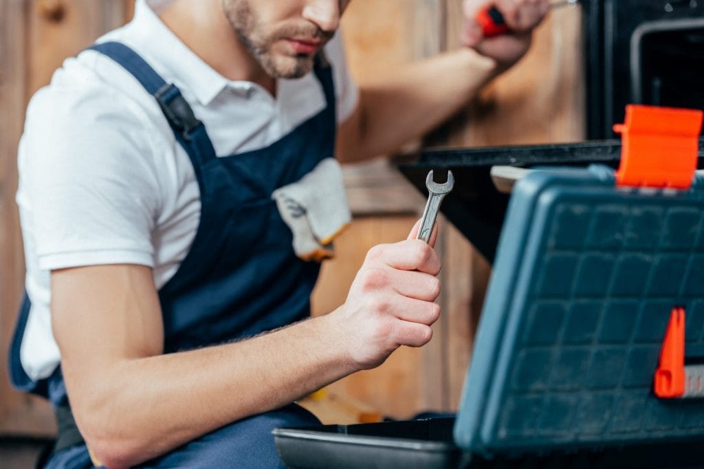 Appliance repair technician holding a wrench beside a toolbox